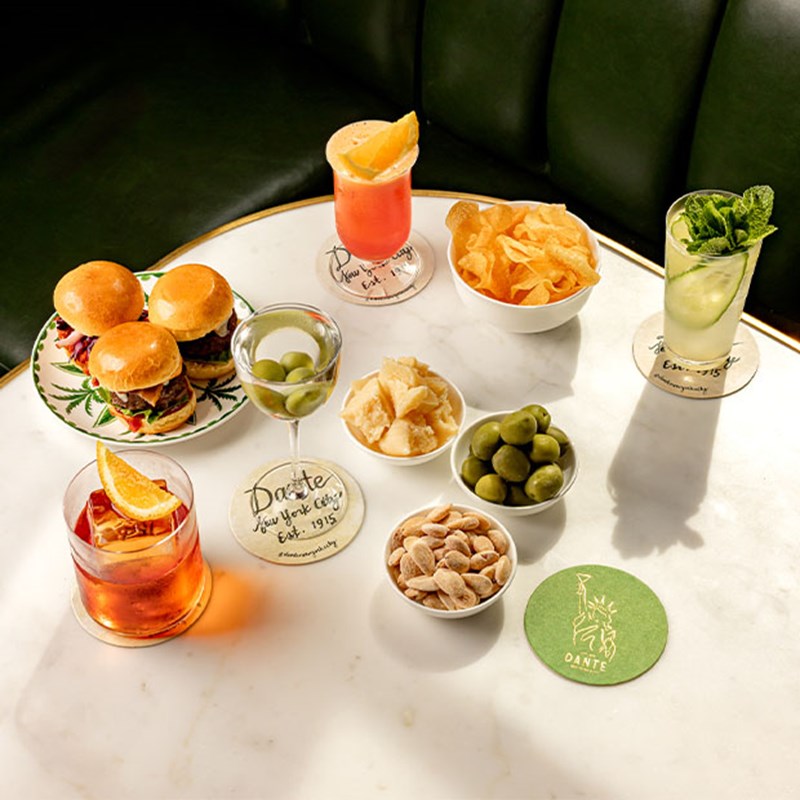 A marble table with sliders, green olives, crisps, nuts, cheese, and an array of colourful cocktails and aperitifs.