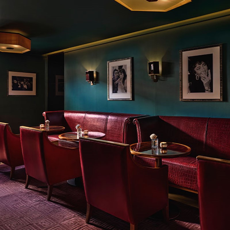 A moody bar interior with red leather armchairs and dark green walls decorated with black-and-white celebrity portraits