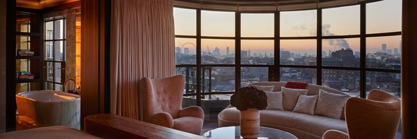 sofas and chairs around a round coffee table, with a view of a sunset over London from the full length window behind