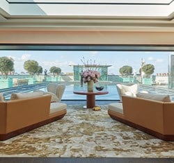 Claridges Penthouse sitting area. A water feature is in the background and a circular wooden table with flowers sits in front of it. A couch and chair sit to the right and left.