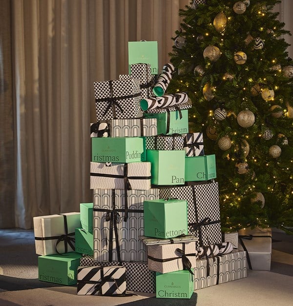 A tall stack of black, white and mint-green wrapped Christmas gifts beside a decorated tree with warm lights.