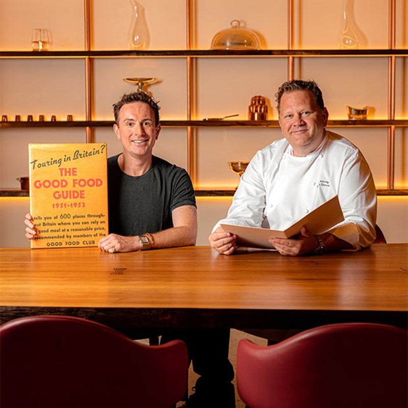 2 chefs sat holding up 'The Good Food Guide 1951-1952.'