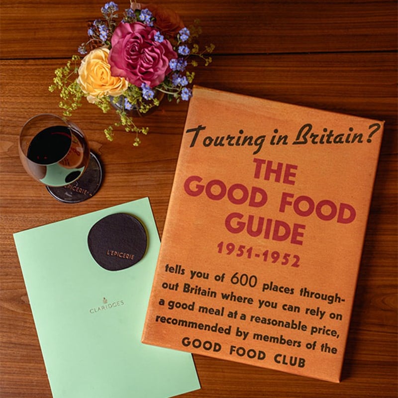 The Good Food Guide 1951-1952 beside a Claridge's menu, a small boquet of flowers and a glass of red wine.