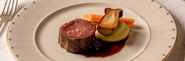 Plate of seared beef fillet topped with sea salt, served with glazed carrot, roasted onion, and king oyster mushroom on a bed of rich jus.