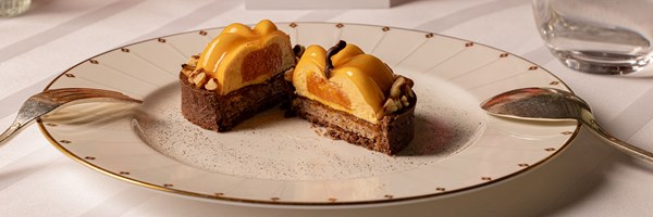 Chocolate tart dessert cut in half, filled with caramel mousse and orange segments, topped with glossy glaze and sprinkled with chopped nuts.