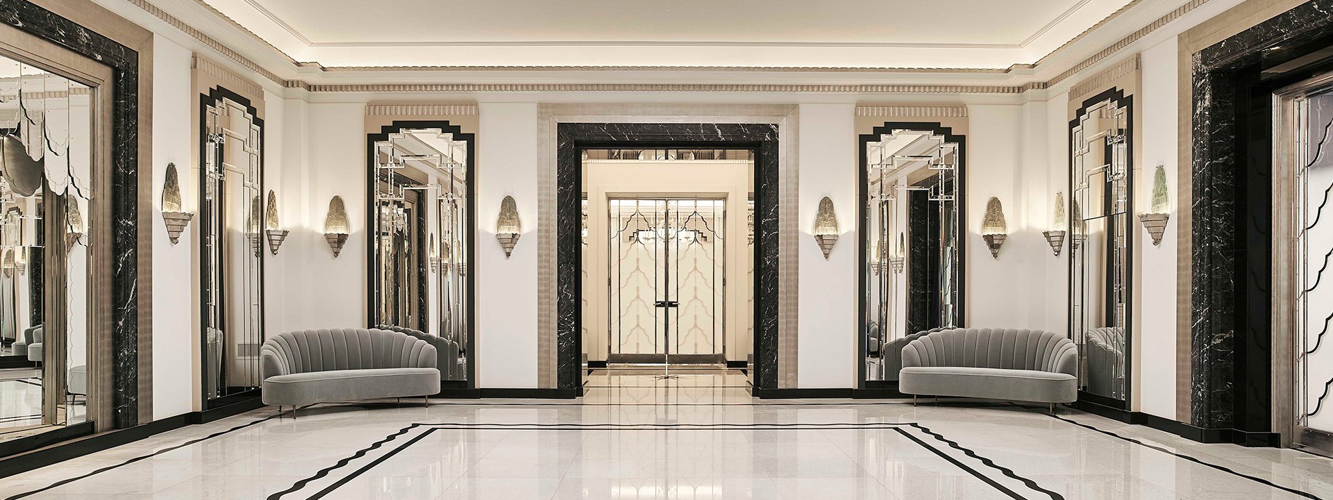 Ballroom reception area in marble and mirrored walls, with two grey sofas in the 1930s style.