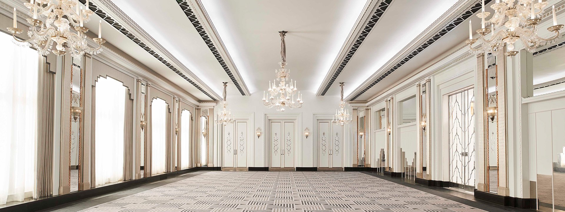 Ballroom with chandeliers, mirrors and carpet in Art Deco style, with gentle lighting that circulates through the space.