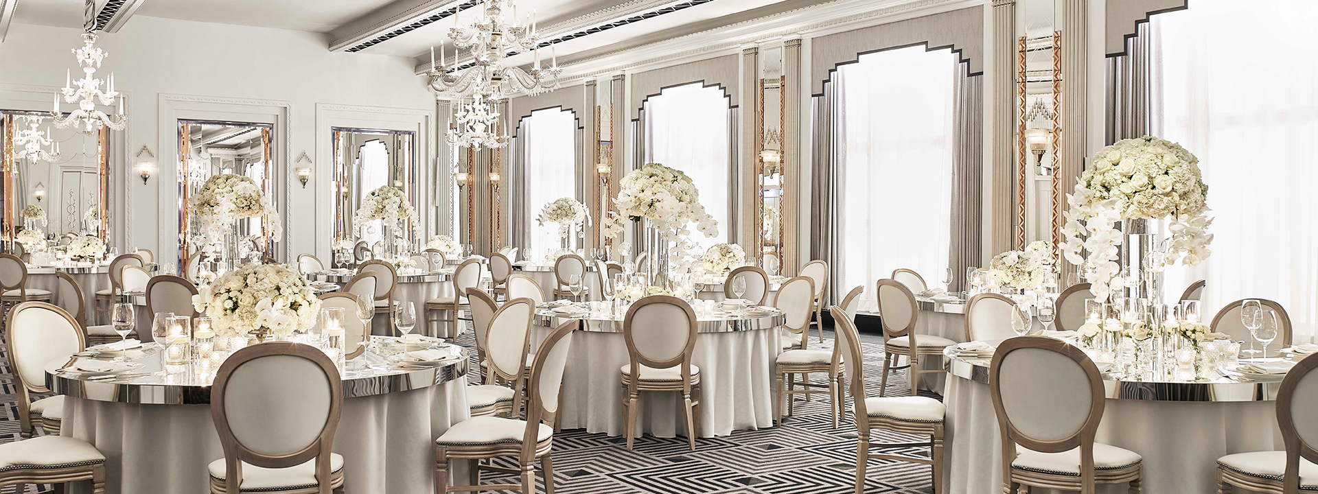 A luxurious hall in Art Deco style, softly lit and enriched with comfortable chairs, and tables with glamorous flowers.