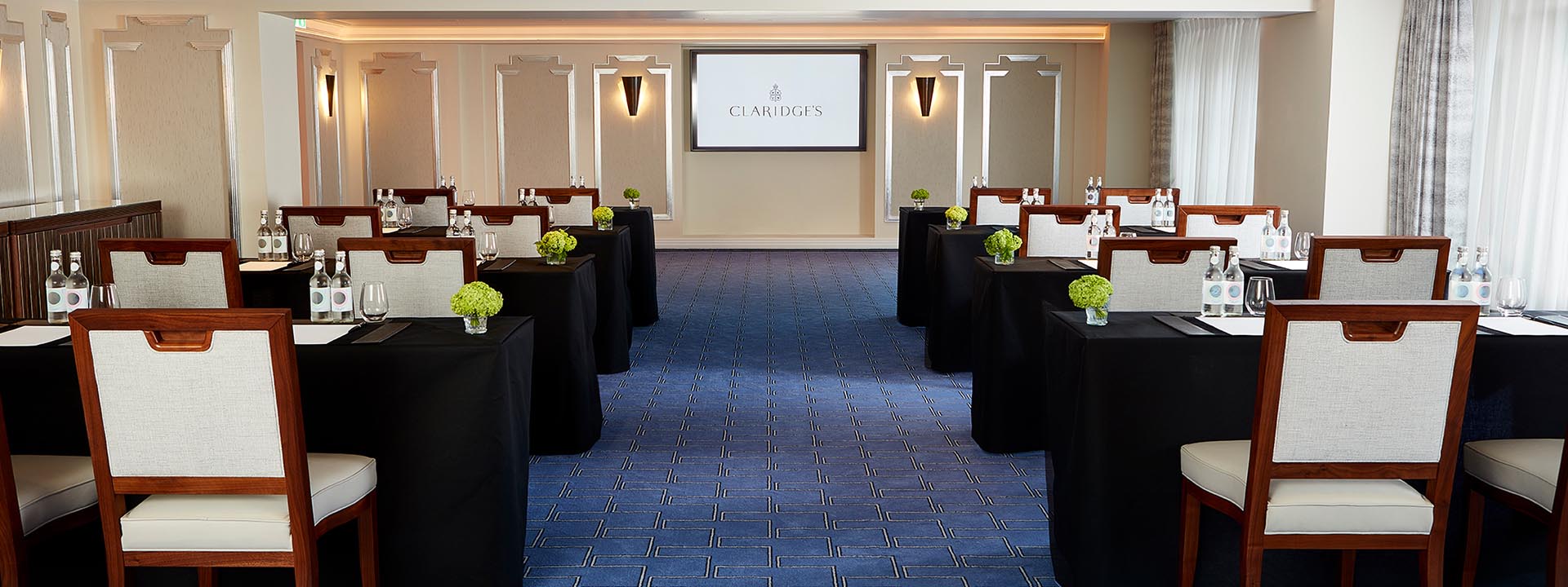 Part of the Clarence Room, in Art Deco design, with comfortable chairs and tables and with a beautiful blue carpet.