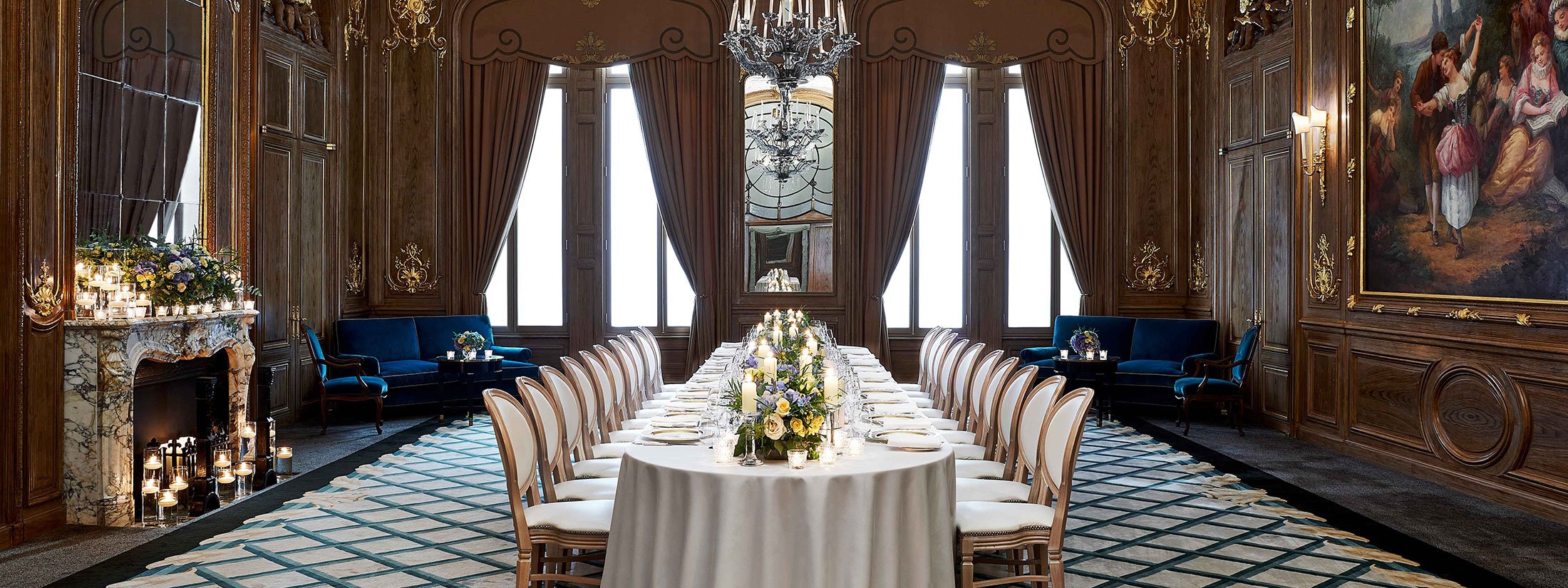 A table setting in the French Salon, surrounded by a marble fireplace, a mural and flower arrangements.