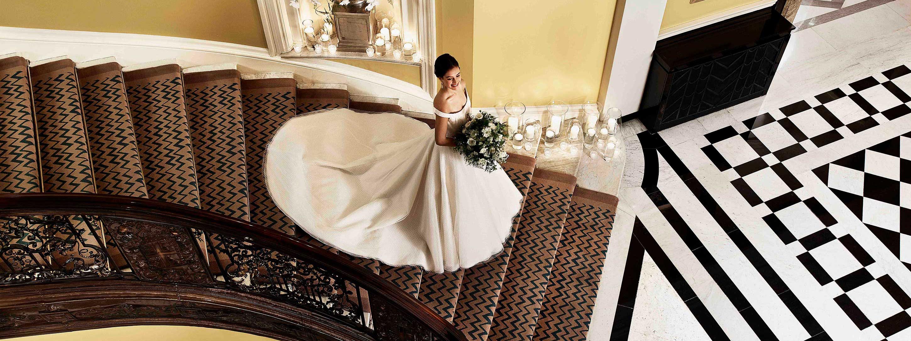 A happy and smiling bride in a magnificent wedding dress walking down the stairs at Claridge's.