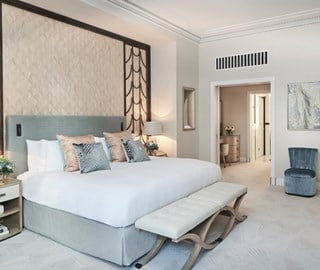 Bedroom with art deco design, one King Bed, velvet blue armchair, and interior in beige colours.