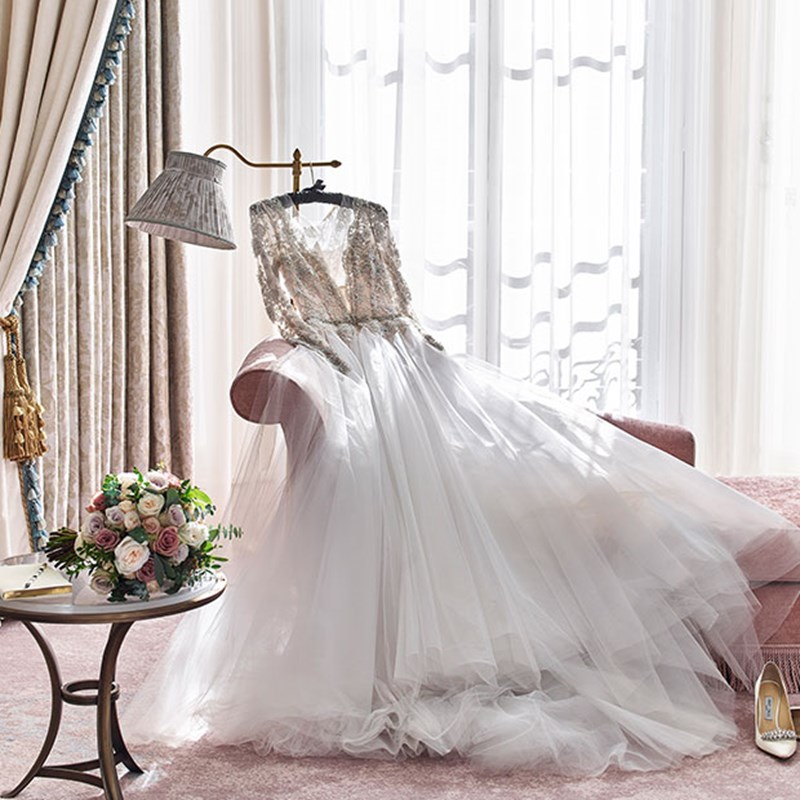 Presentation of a stunning wedding dress hung in a romantic interior with floral arrangements.