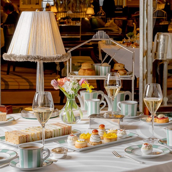 The Foyer and Reading Room afternoon tea set up with finger sandwiches and pastries set on the table, scones with jam and cream in the background and full glasses of champagne