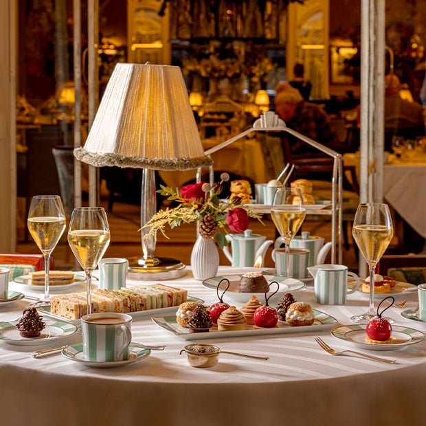 a sumptuous tea setting in an elegantly decorated room, complete with classic tea service, Champagne, and seasonal floral arrangements, offering a warm, inviting atmosphere for festive gatherings.