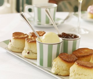 Delicious scones with jam and clotted cream, served on a mint green and white plate.