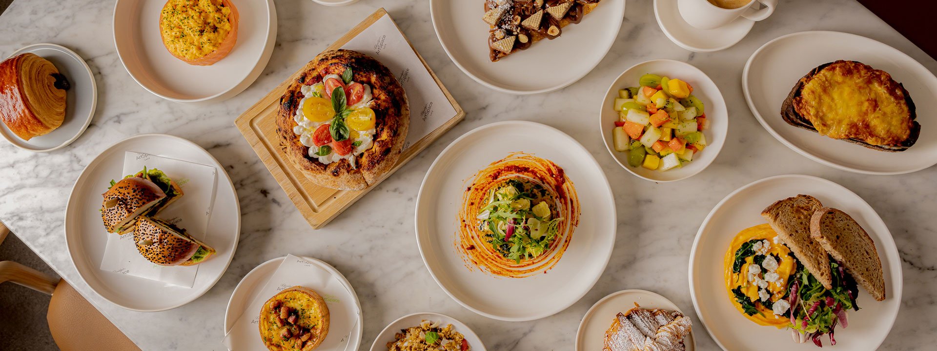Marble table at Claridge’s ArtSpace Café set with a colourful variety of dishes including pastries, sandwiches, salads, fruit, and coffee.