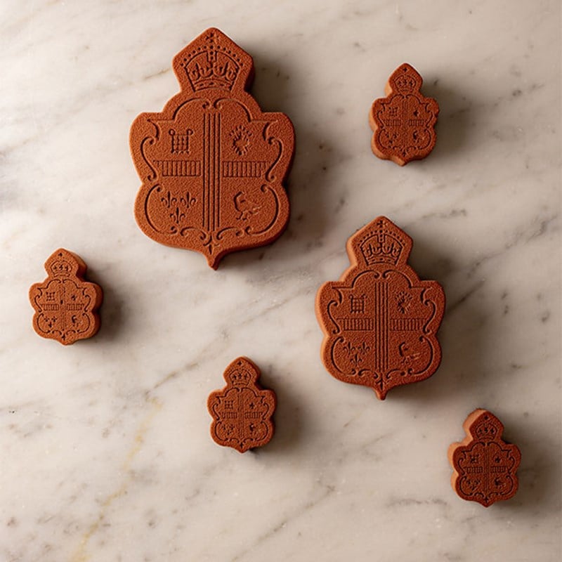 A selection of intricately embossed chocolate biscuits in various sizes, bearing the Claridge’s crest, artfully arranged on a marble surface.