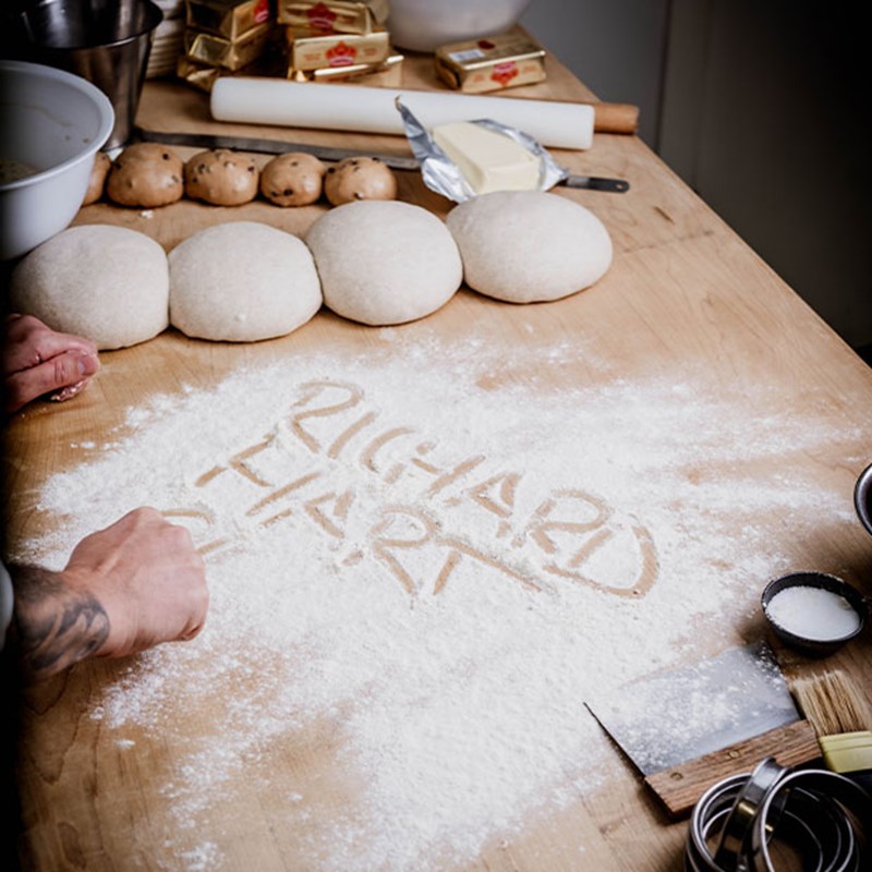 Dough balls and baking ingredients are arranged on a floured surface, with