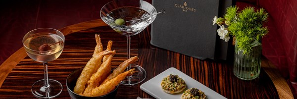 Claridge's bar, 2 cocktails in coupes, menu, white and green flowers, fried prawns and caviar blinis on wooden table
