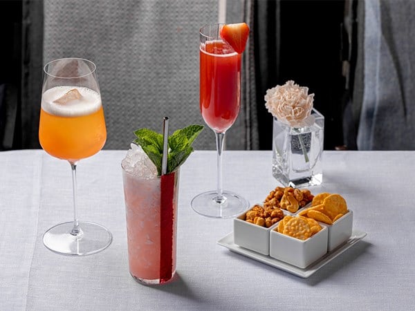 Table at Claridge's bar terrace with three cocktails, bar snacks and a single flower in a vase.