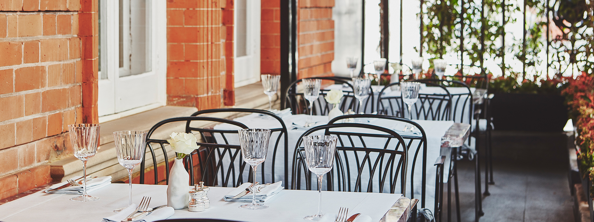 Elegant crystal glasses arranged on tables from the terrace bar at Claridge's, along with floral arrangements.