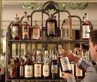 A view of a bartender selecting from a shelf of vintage whiskeys at Claridge's Bar.