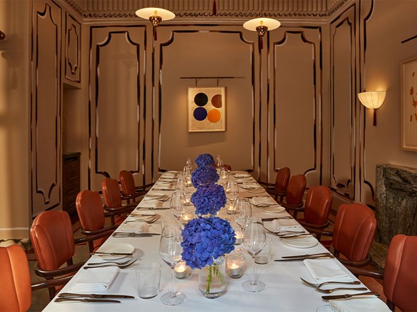 A long private dining table set for a formal meal with deep red chairs, white tablecloth, and vases of purple hydrangeas in an elegant room with decorative panelled walls and soft lighting.