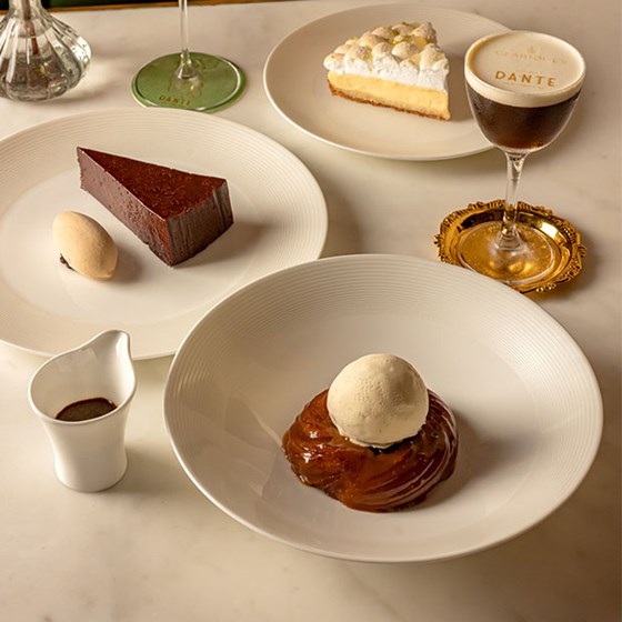 A table setting with three desserts—vanilla ice cream with chocolate sauce, a slice of chocolate cake with ice cream, and a lemon tart—served alongside an espresso martini.