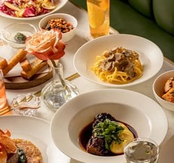 A table filled with Italian dishes, including truffle pasta, braised beef with polenta, salad, breadsticks, and drinks, with a rose in a glass vase at the center.