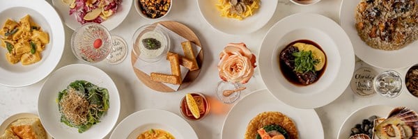 Overhead view of an elegant dining table at Claridge’s, set with multiple autumn-inspired Italian dishes including pasta, risotto, braised meat, seafood, salad, and cocktails.”
