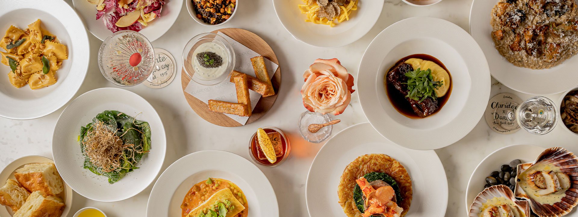 Overhead view of an elegant dining table at Claridge’s, set with multiple autumn-inspired Italian dishes including pasta, risotto, braised meat, seafood, salad, and cocktails.”
