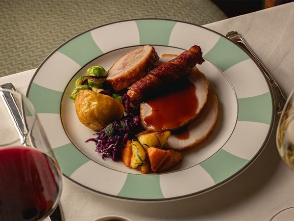Festive roast turkey plate with vegetables and gravy on mint-striped china beside red wine.
