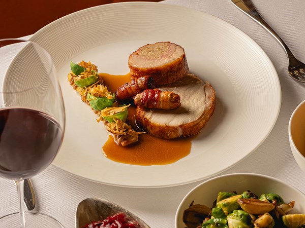 Roast turkey with stuffing, pigs in blankets and sprouts on a white plate with gravy and red wine.