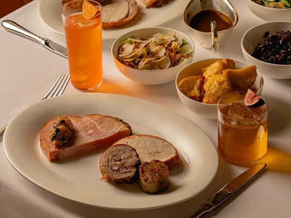 Sliced roast with stuffing, pigs in blankets and sprouts in gravy beside a glass of red wine.