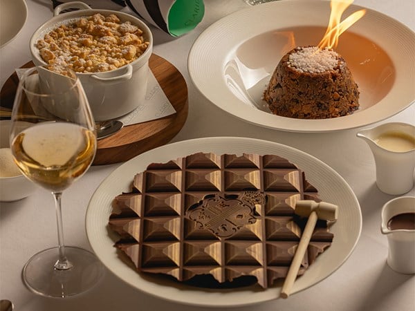 Flaming Christmas pudding, crumble and chocolate slab dessert with wine on a white table.