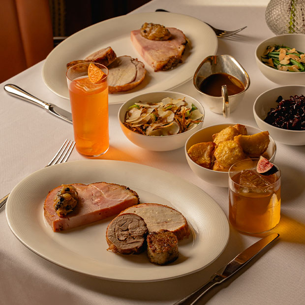 Festive roast pork with trimmings, side dishes, gravy, and cocktails on a white tablecloth.