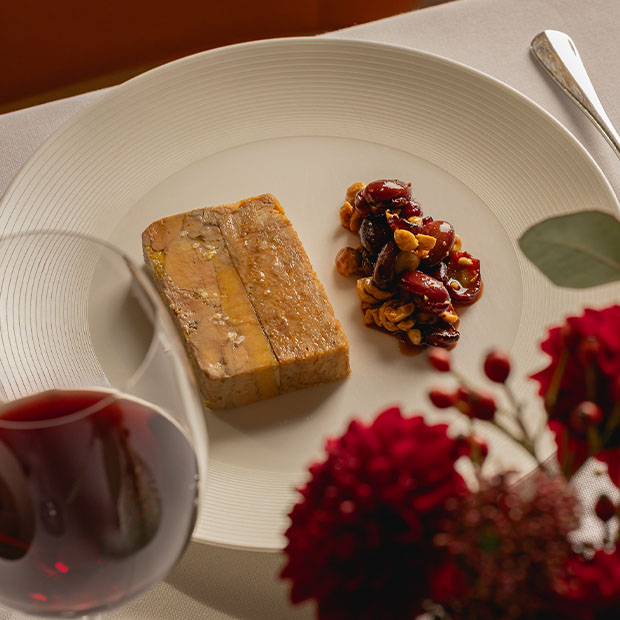 Foie gras terrine with a dried fruit and nut garnish, served beside a glass of red wine.