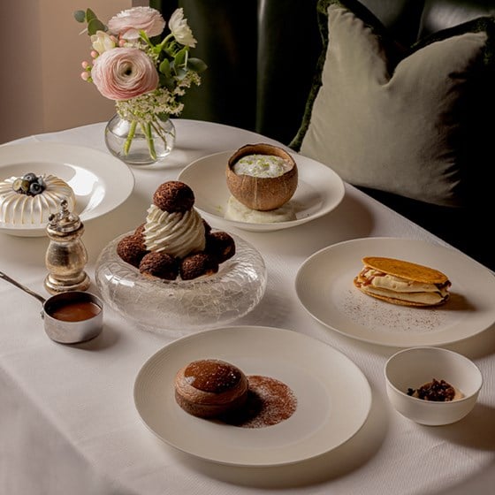 A refined dessert selection elegantly plated on a white tablecloth with a floral arrangement.