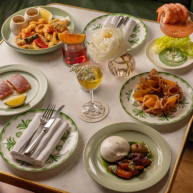 An elegant table spread with seafood, pasta, burrata, salads, cocktails, and green-rimmed plates.