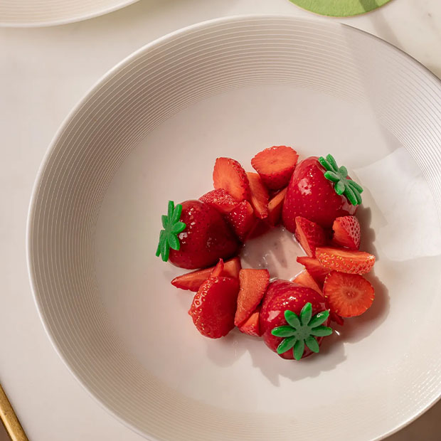 A white bowl holding sliced strawberries arranged in a ring with a light sauce at the centre.