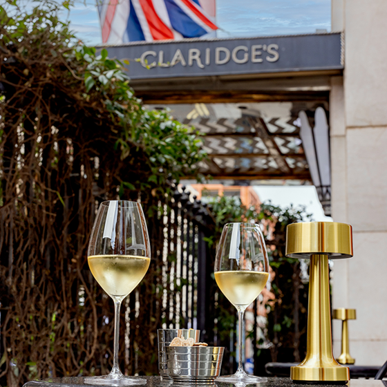 Two glass of white wine on an outdoor terrace with the Claridge's sign in the background and the British flag beyond.