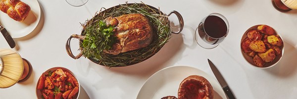 Claridge's Restaurant birds eye view of glass of red wine, roast poratoes, yorkshire pudding iwtha knife, roast carrots, roast chicken on oval dish with green herbs, and a bread roll