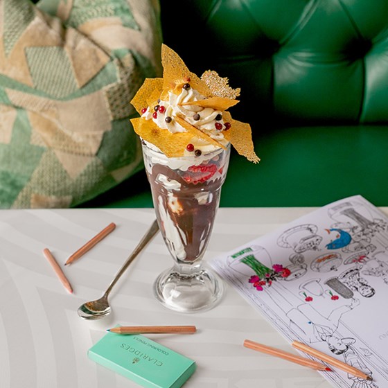 A view of a decorated hot chocolate from the children's menu at Claridge's, with colouring books and crayons next to it.