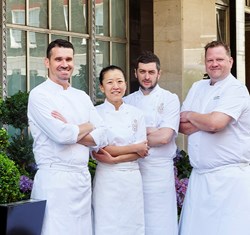 Four chefs, smiling and standing confidently outside Claridge's dressed in professional white uniforms.