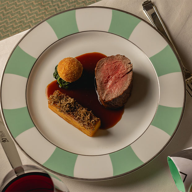 Sliced beef fillet served with potato gratin, a crispy croquette, and red wine sauce.