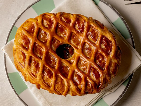 Golden lattice-topped pastry served on a napkin-lined plate with green-and-white detailing, showcasing crisp layers and a glossy finish at the centre.