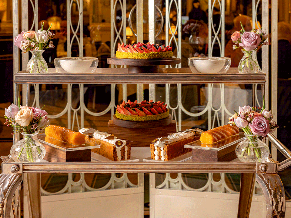 Two-tier dessert trolley with strawberry tarts, pastries and cakes, styled with small floral arrangements in an elegant dining room.