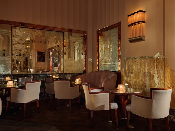 Art Deco–style lounge at Claridge’s The Fumoir, featuring plush upholstered chairs and banquette seating, marble accents, mirrored panels with etched designs, and softly lit tables.