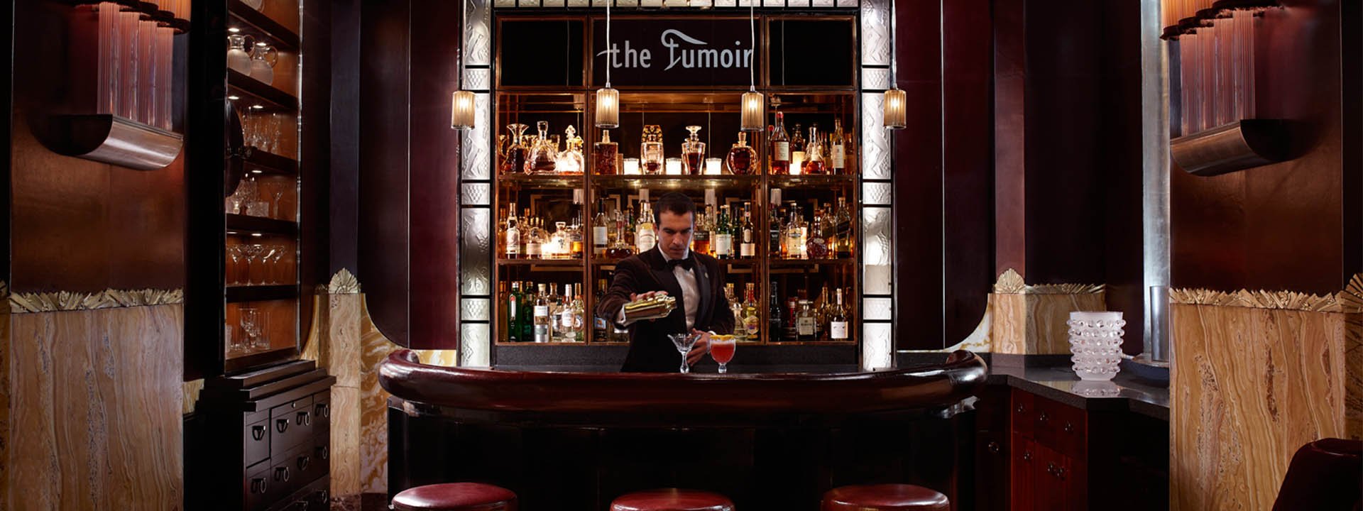 A stylish bartender pours a drink from a shaker into a cocktail glass at Claridge's Bar.